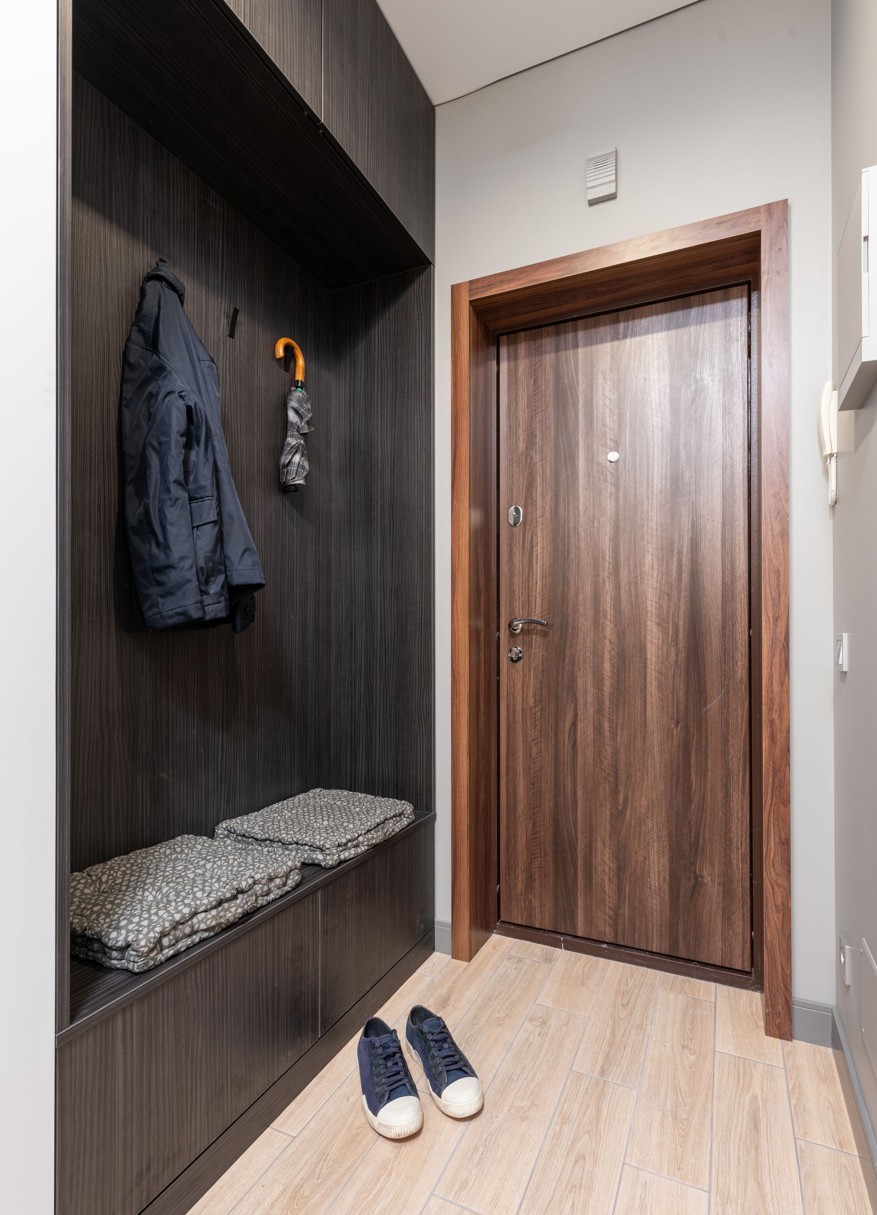 Eingangsbereich mit Jacke und Schirm an Haken, Sitzbank, Schuhen und freier Wohnungstür
