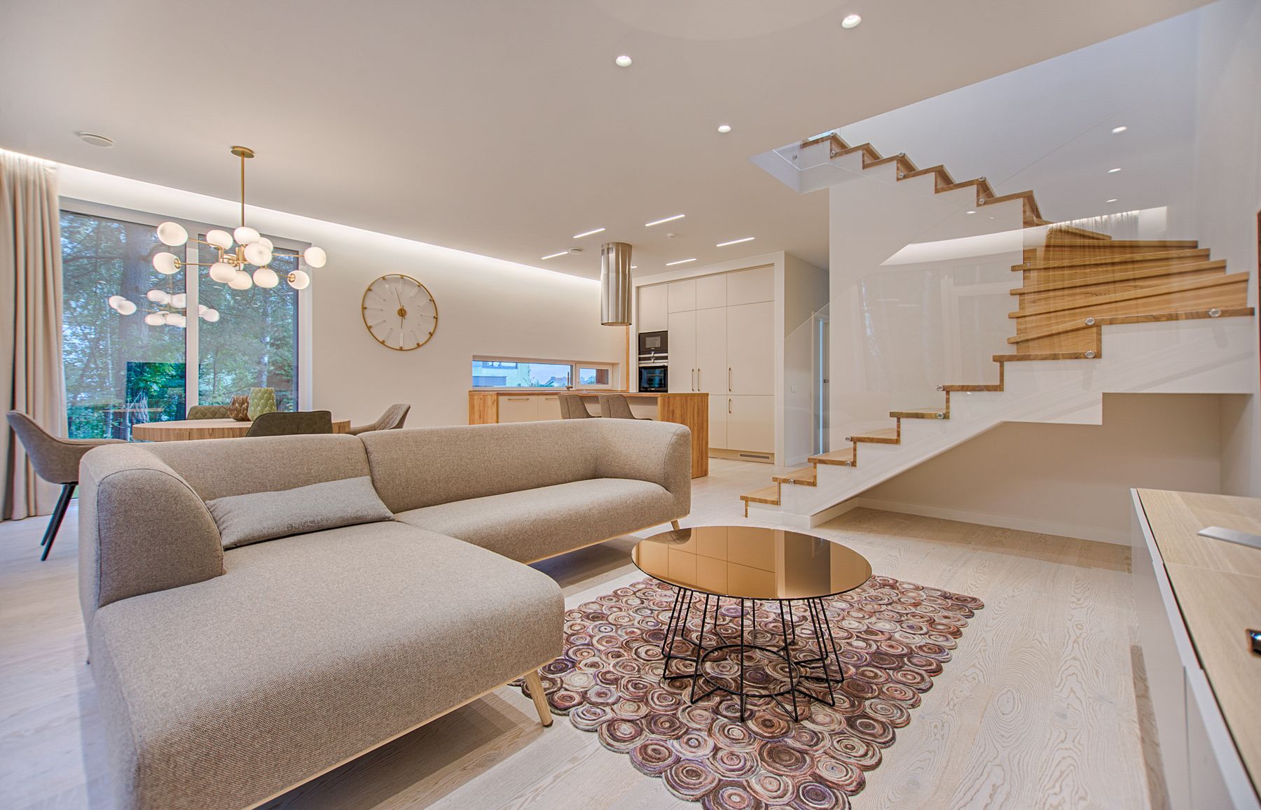Helles Wohnzimmer mit grauem Sofa, rundem Couchtisch und offener Holztreppe